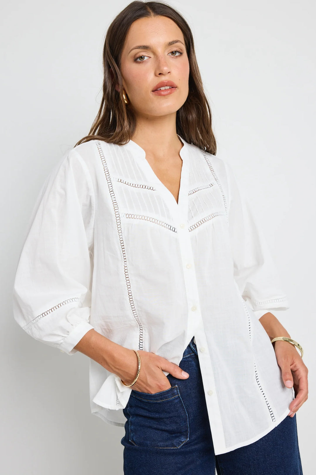 A woman wearing a white ornamental pintuck shirt with lace inserts and puff sleeves, paired with blue jeans.