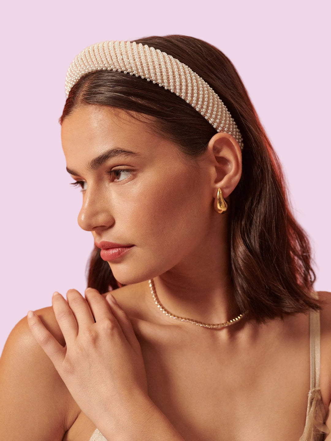 Woman wearing a pearl headband and gold earrings against an orange background