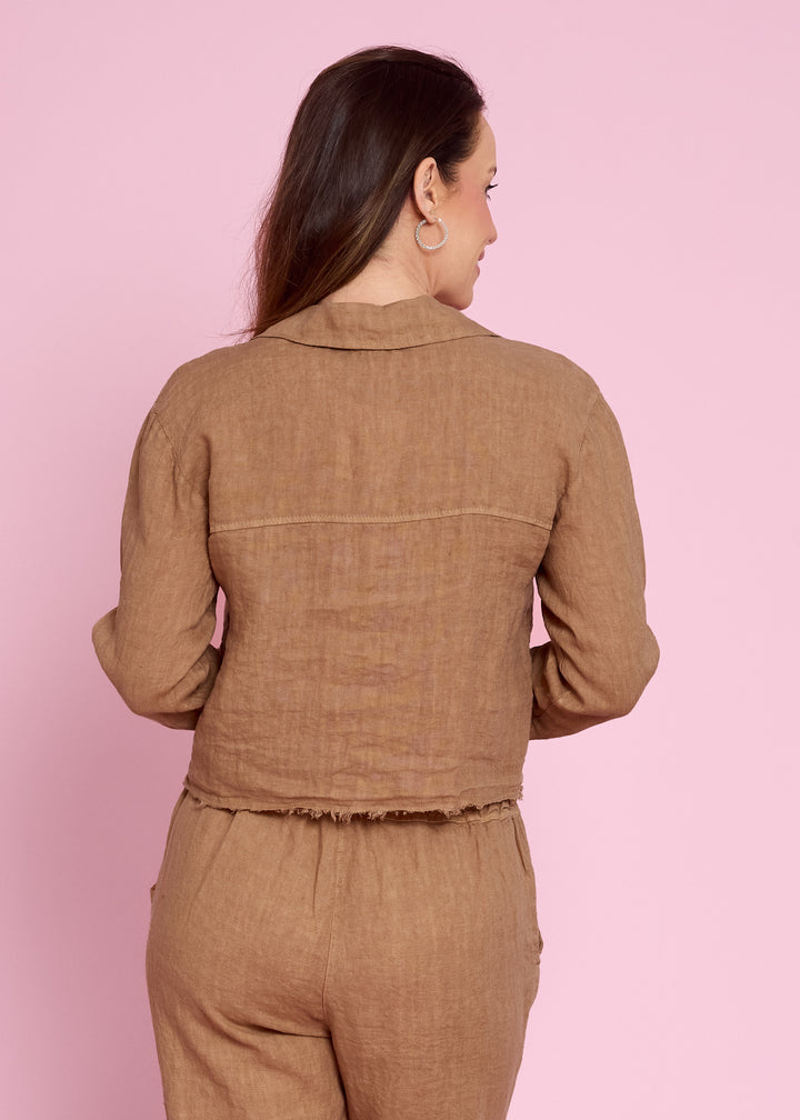 A woman shown from the back wearing a brown linen long-sleeve cropped jacket and matching trousers against a solid pink background.