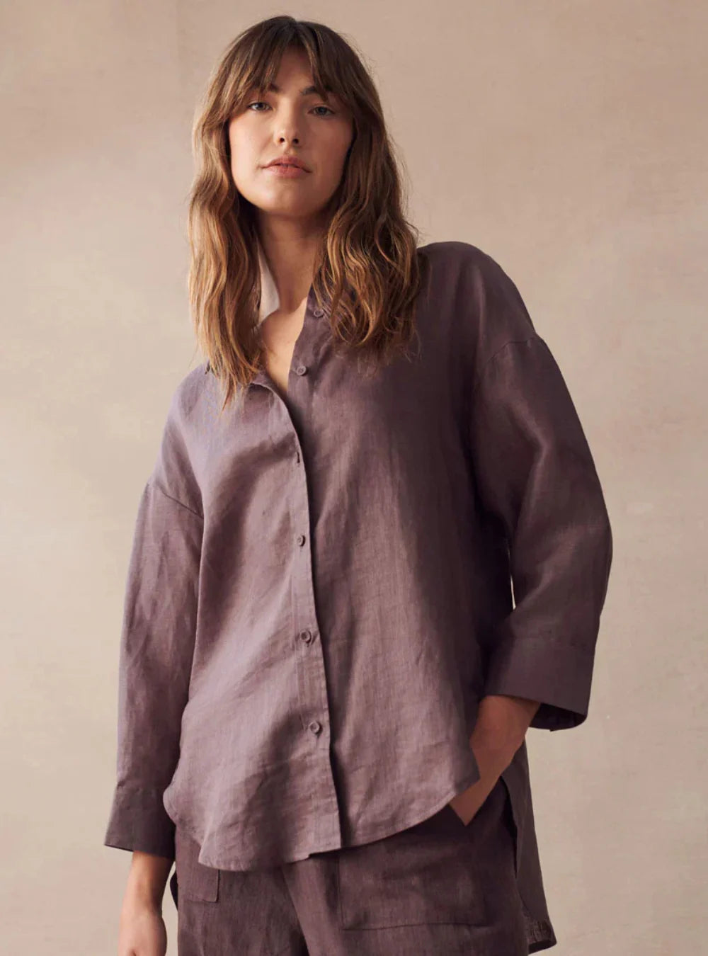 Woman wearing a loose-fitting, long-sleeve shirt and pants in a neutral setting