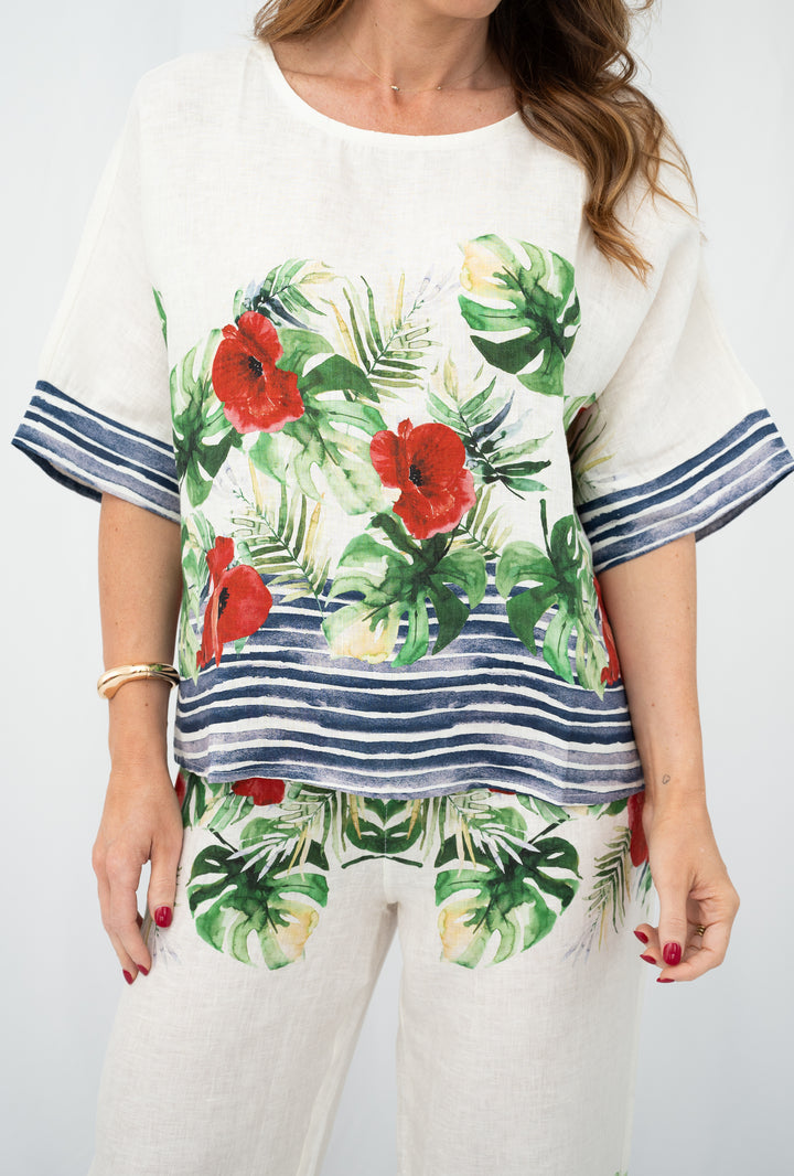 Woman wearing a white outfit with tropical floral patterns on a plain background Woman wearing Italian linen top with tropical floral and navy stripe print.
Close-up of botanical print linen top from the Capri Coast Collection.
White linen top styled with matching printed linen pants.
