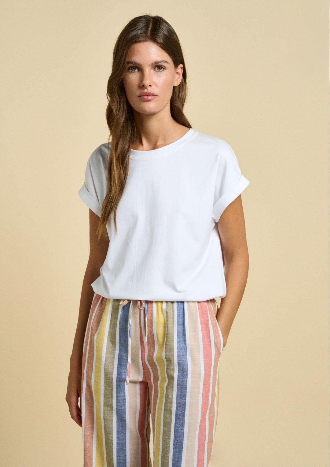 Woman wearing a white top and colorful striped pants on a beige background