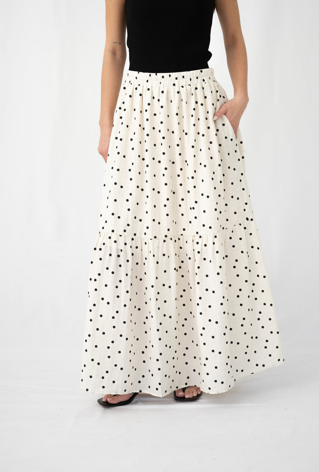 Woman wearing a tiered cream maxi skirt with black polka dots and elastic waistband, paired with a black top