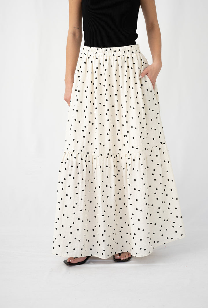 Woman wearing a tiered cream maxi skirt with black polka dots and elastic waistband, paired with a black top