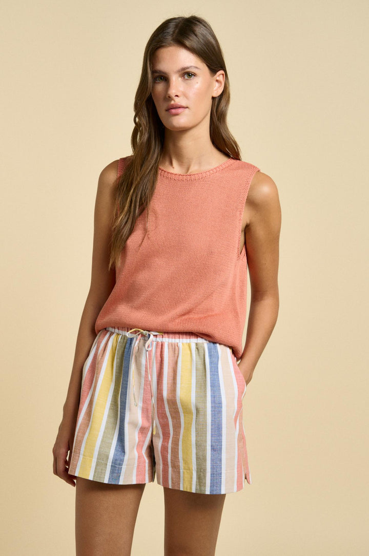 Woman wearing a sleeveless orange top and colorful striped shorts on a beige background