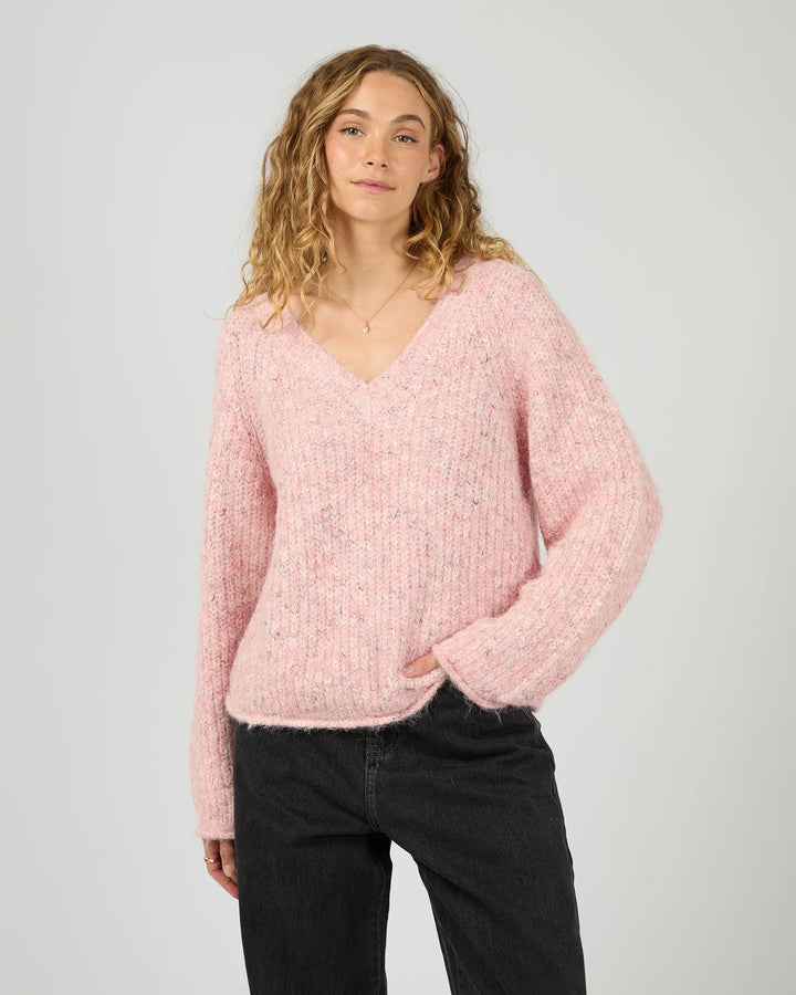 Woman wearing a pink sweater and black pants on a plain background