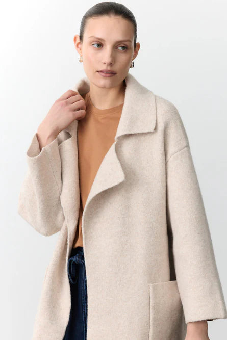 Woman wearing a beige coat over a brown top and blue jeans on a white background
