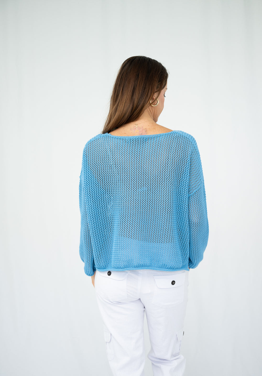 Woman wearing a blue sweater and white pants on a plain background
