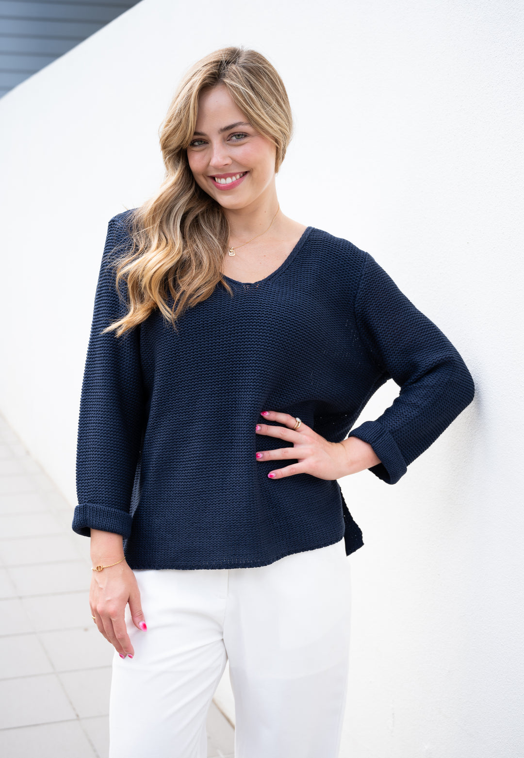 Woman wearing a navy blue sweater and white pants against a light background