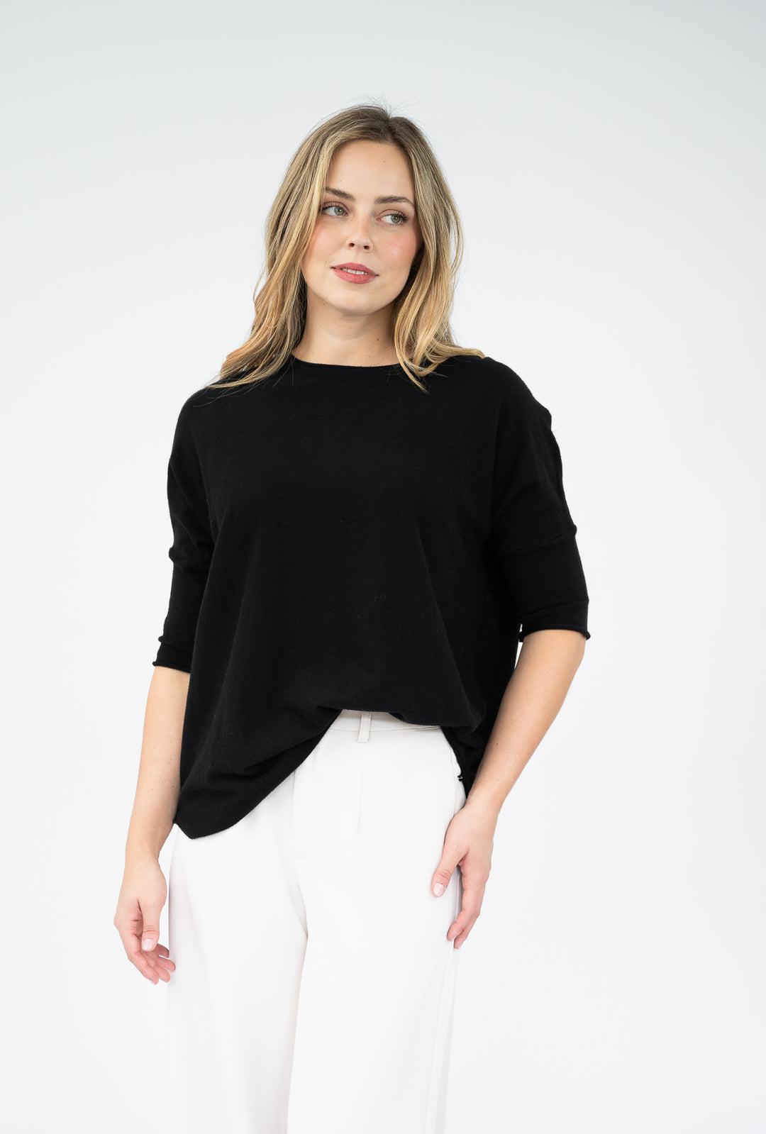 Woman wearing a black top and white pants against a white background