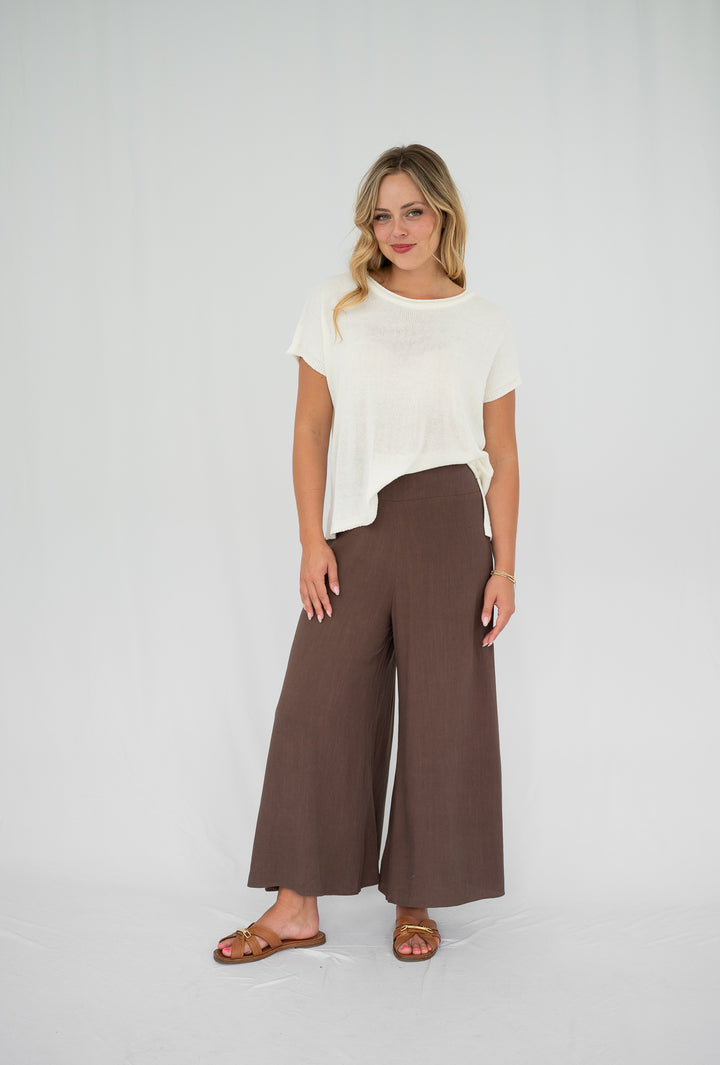 Woman wearing a white top and brown wide-leg pants on a white background