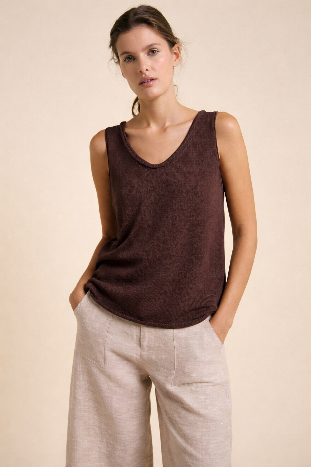 Woman wearing a brown sleeveless top and beige pants against a beige background