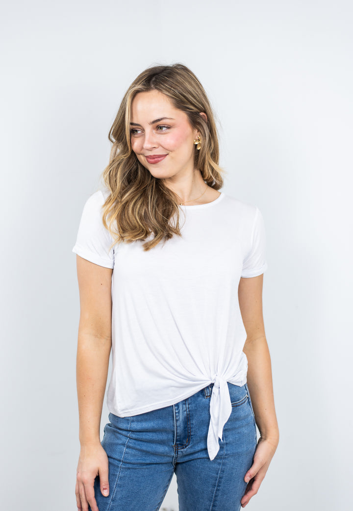 Woman wearing a white modal tee with cuffed sleeves and tie-front detail, styled with light denim jeans — breathable travel top for summer.