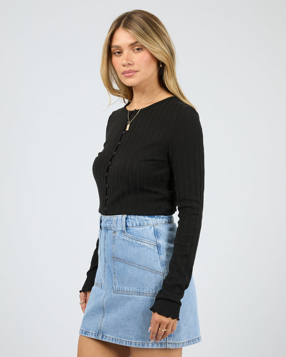 Woman wearing a black long-sleeve top and denim skirt on a white background