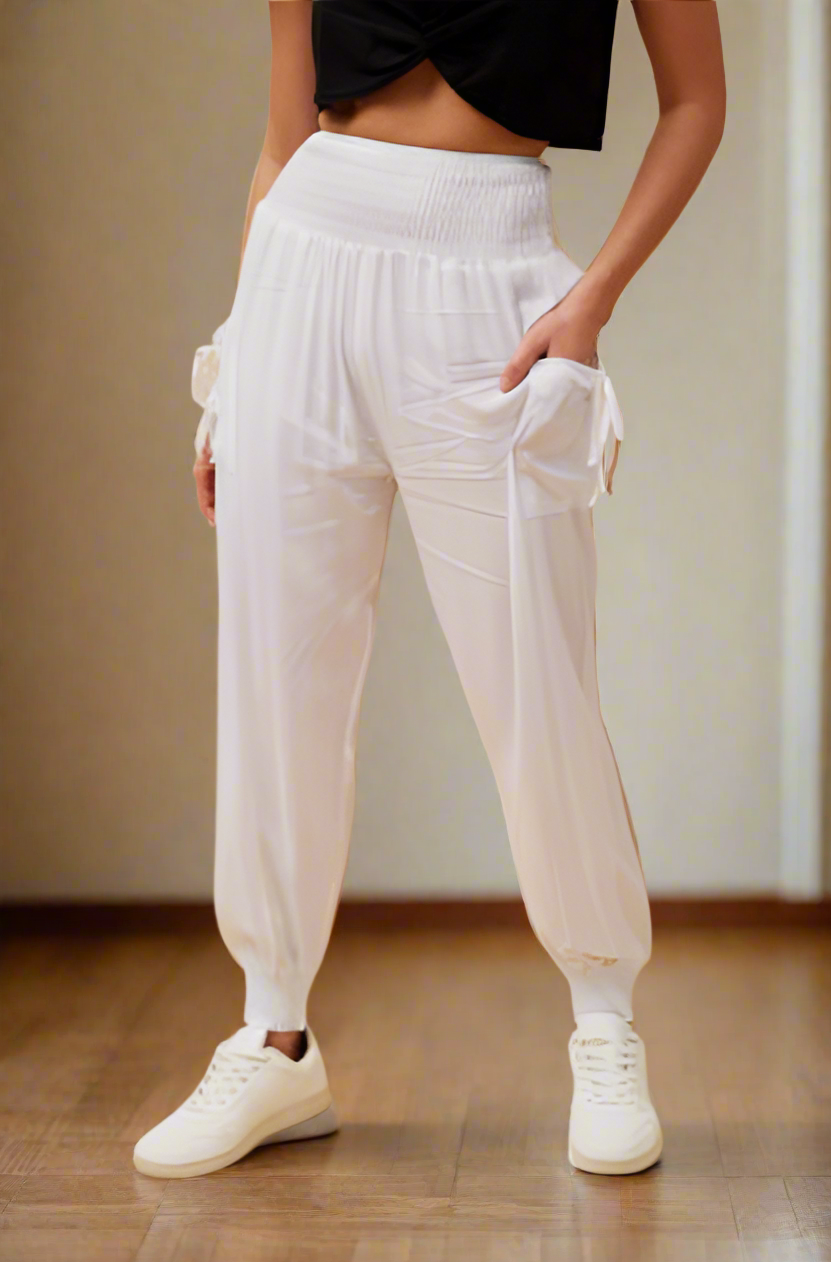 White high-waisted jogger pants with side pockets and drawstring details, worn by a model with a black crop top and white sneakers.