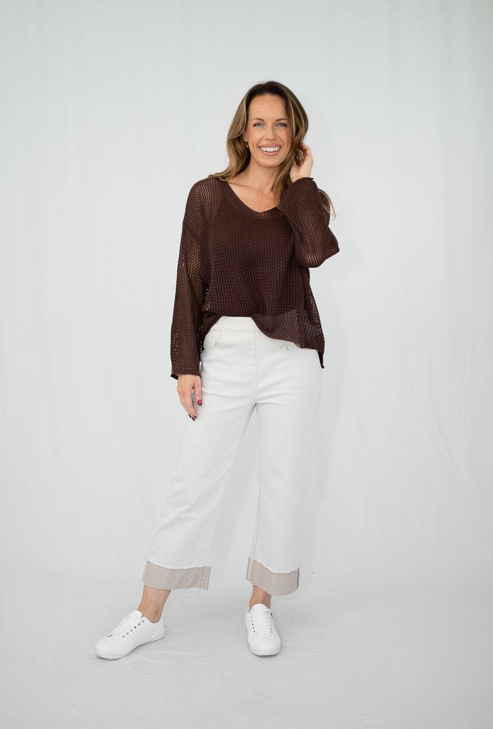 Woman wearing a brown top and white pants on a plain background