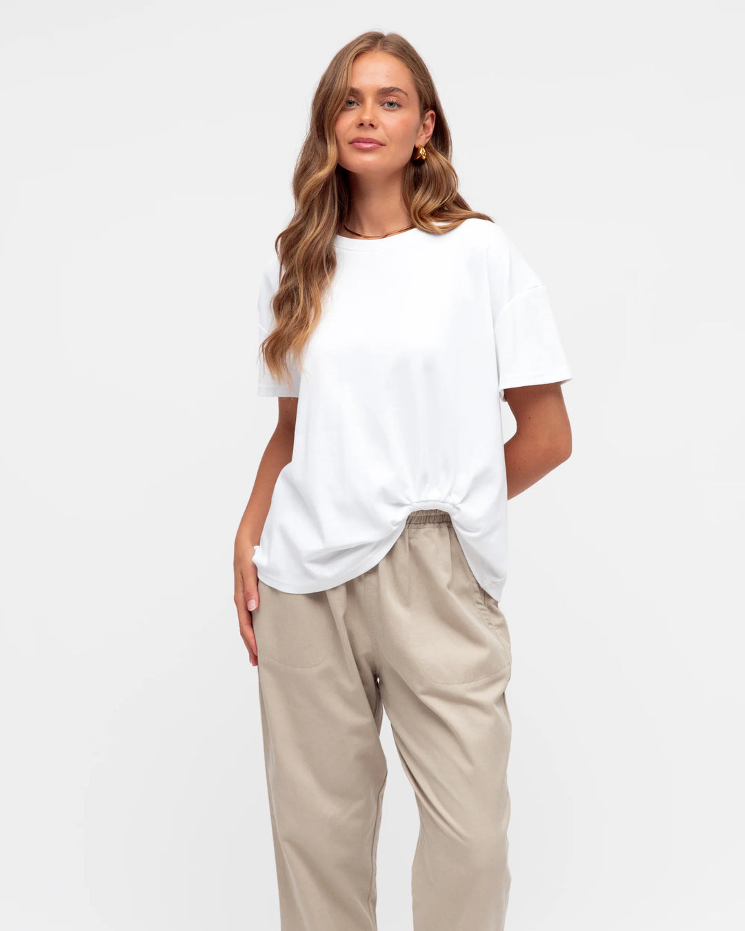 Woman wearing a white t-shirt and beige pants on a plain background