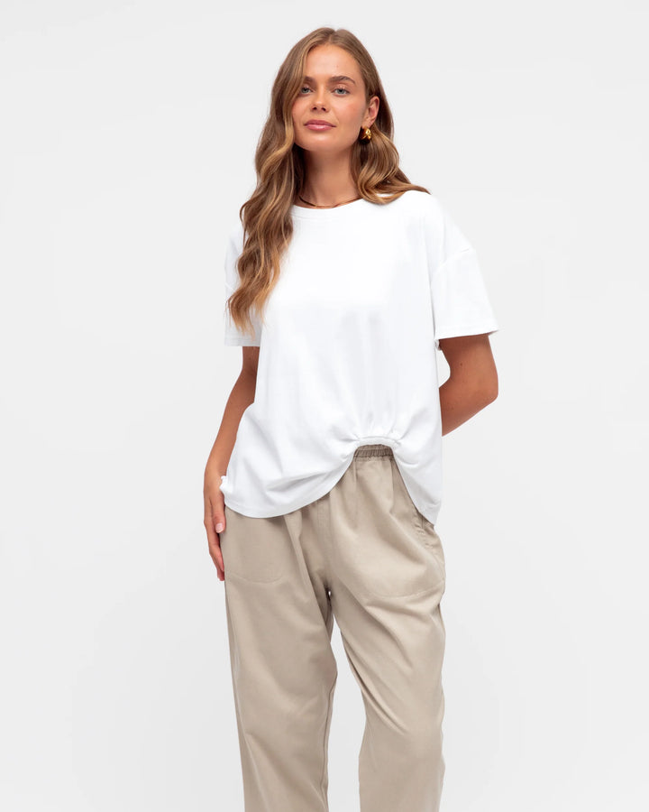 Woman wearing a white t-shirt and beige pants on a plain background