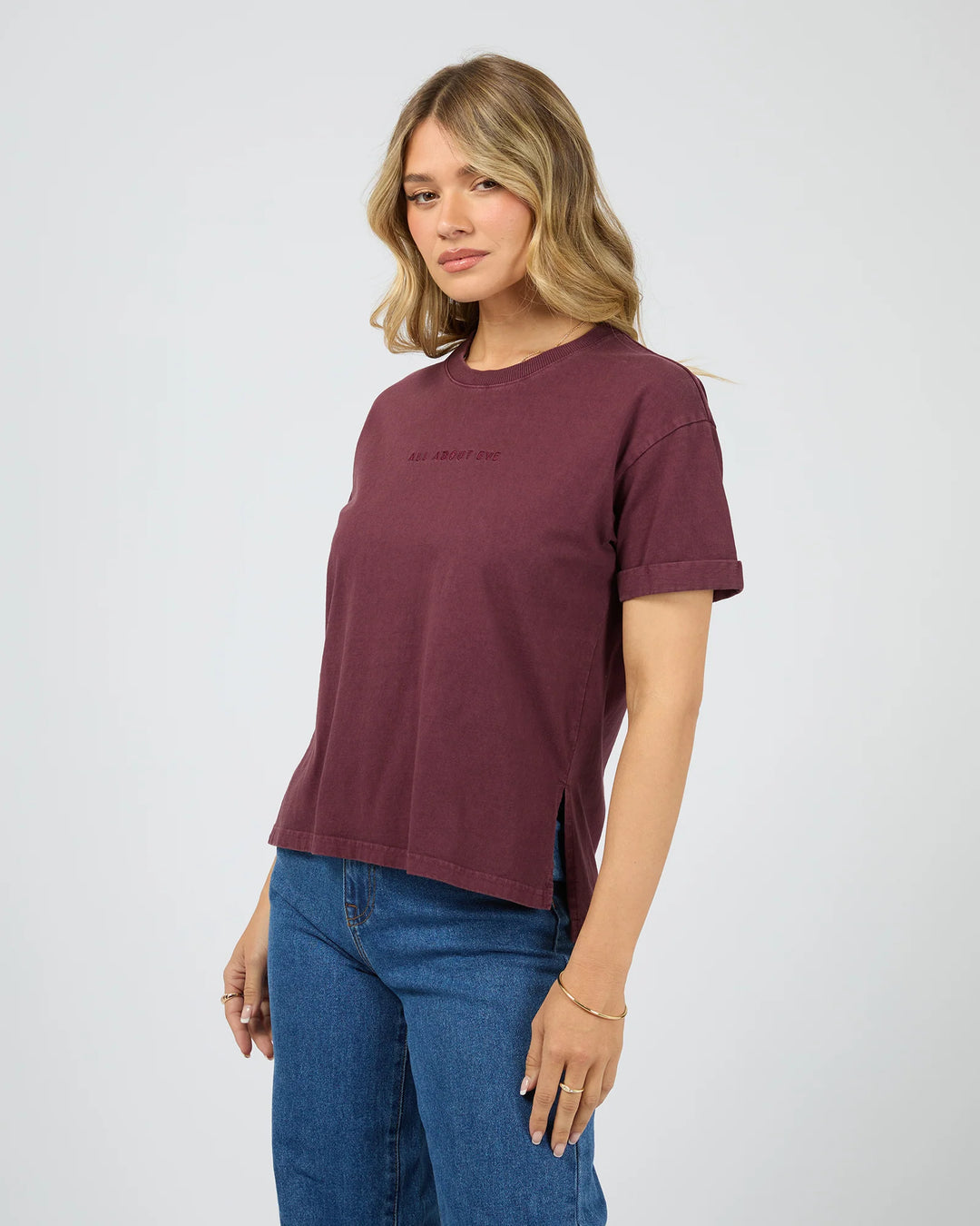 Woman wearing a maroon t-shirt and blue jeans on a white background