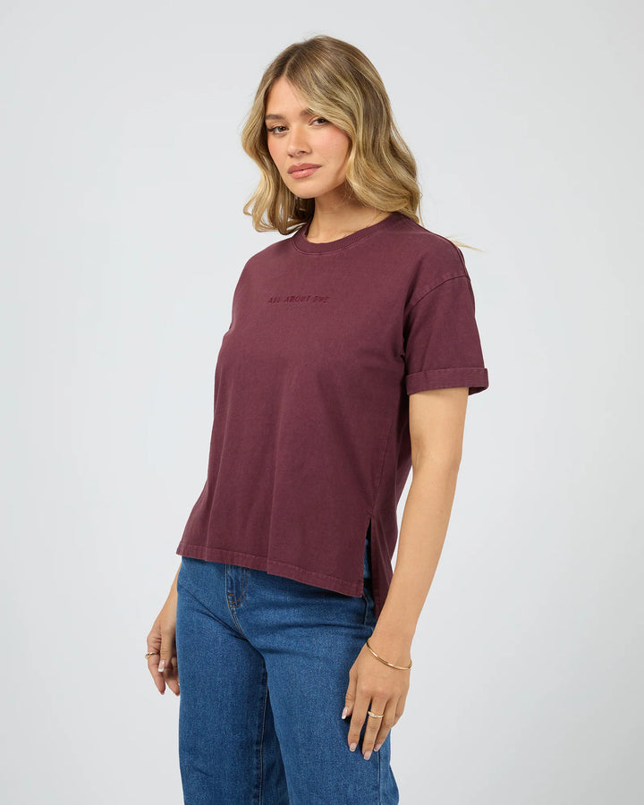 Woman wearing a maroon t-shirt and blue jeans on a white background