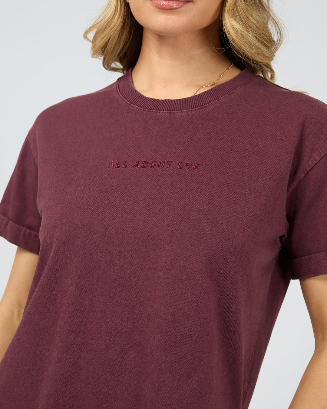 Maroon t-shirt with text worn by a person on a light gray background