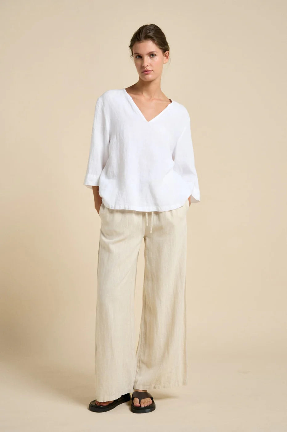 Woman wearing a white blouse and beige pants against a beige background