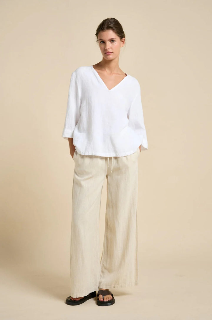 Woman wearing a white blouse and beige pants against a beige background