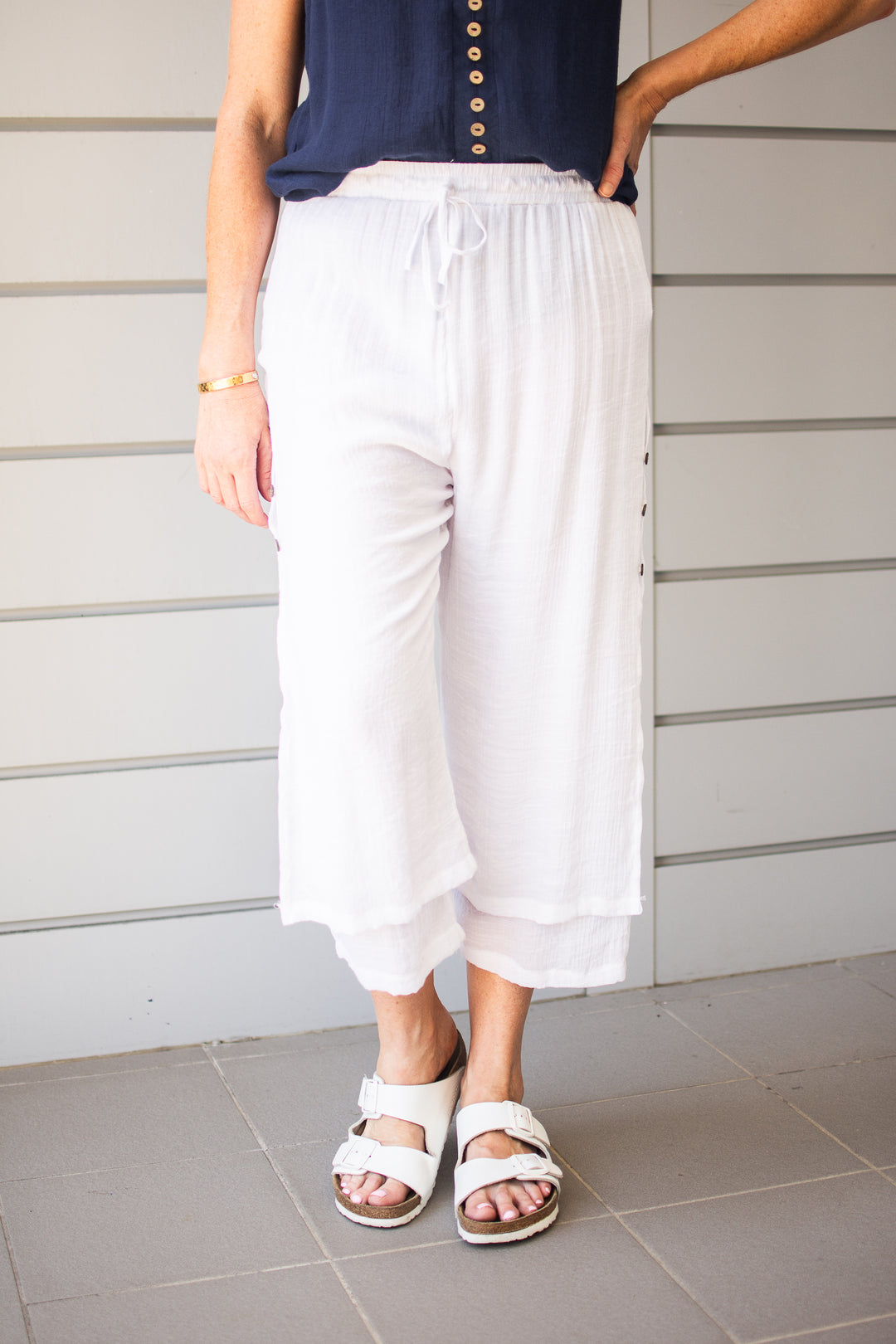 Person wearing white pants and sandals standing against a neutral background