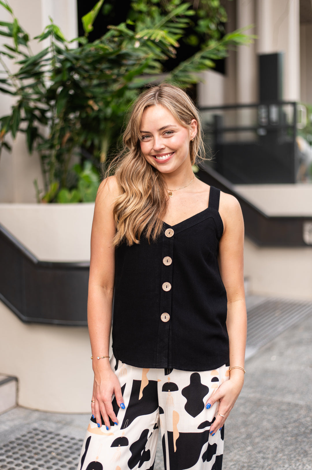 Woman wearing a black sleeveless top with buttons and a patterned skirt outdoors.