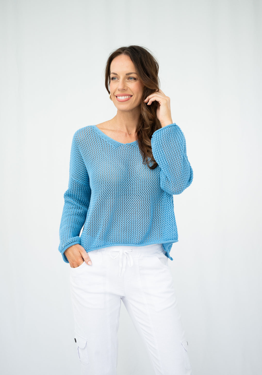 Woman wearing a blue sweater and white pants against a light gray background