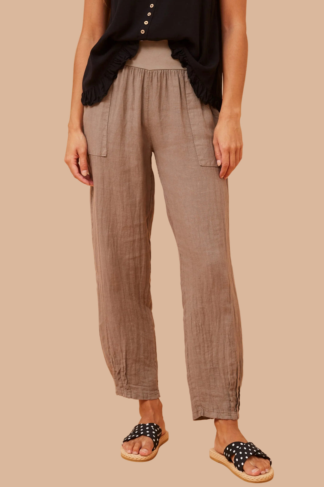 Person wearing brown pants and black sandals on a beige background