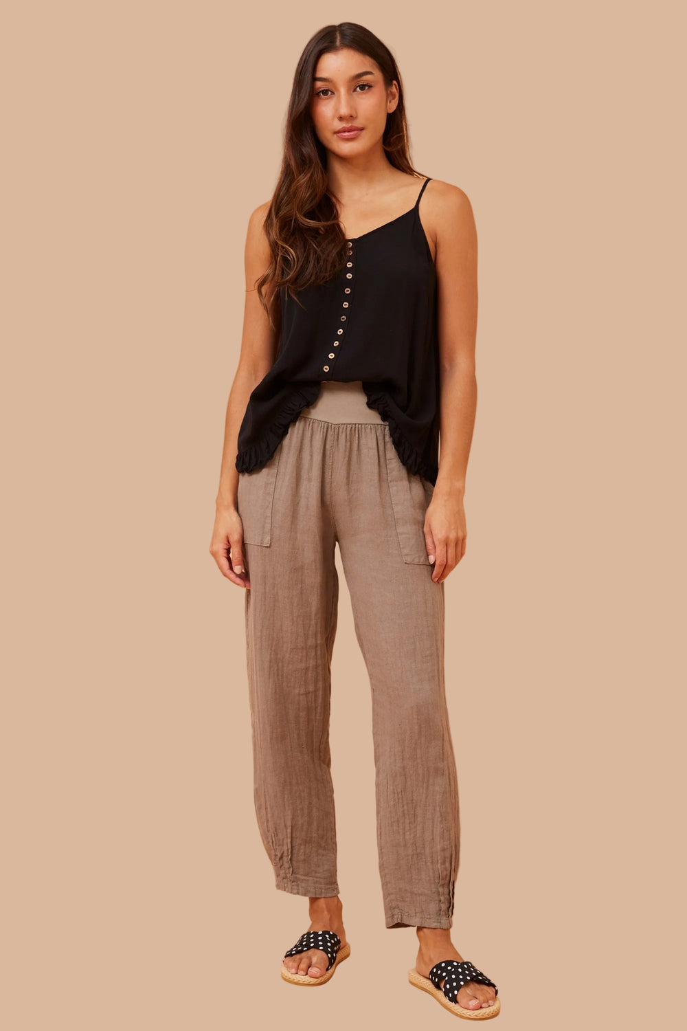 Woman wearing a black sleeveless top and brown pants on a beige background