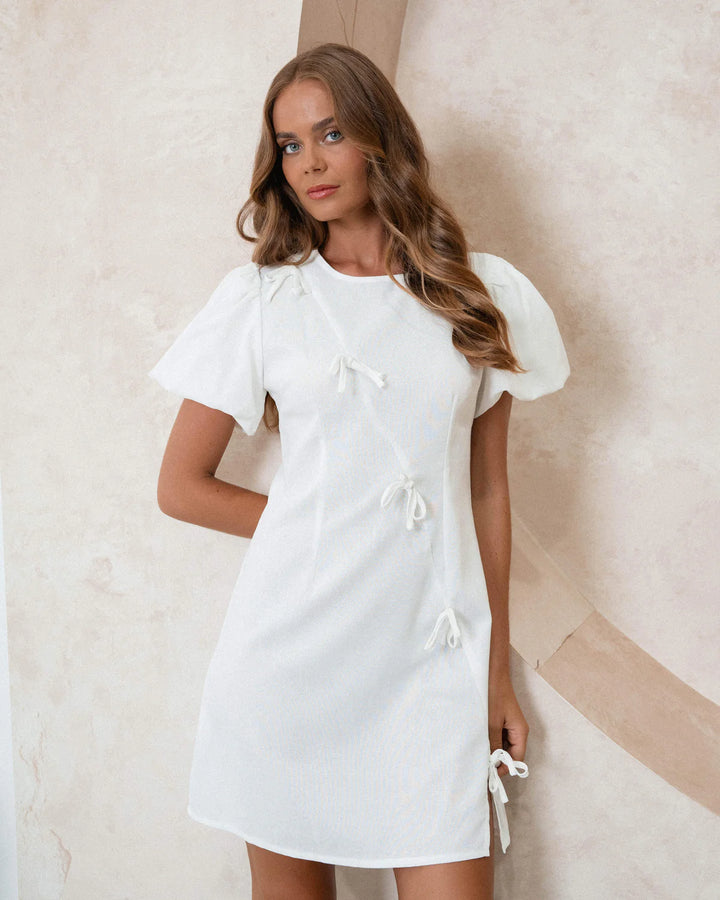Woman wearing a white dress with puffed sleeves against a neutral background