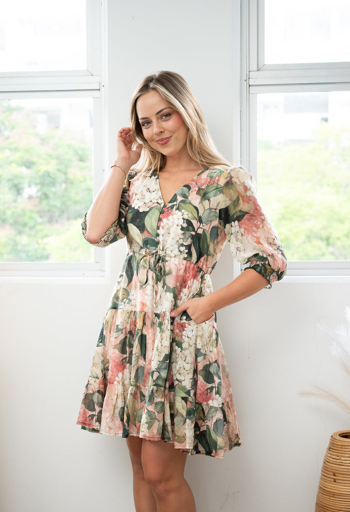 Woman wearing a floral dress standing in a bright room with large windows.