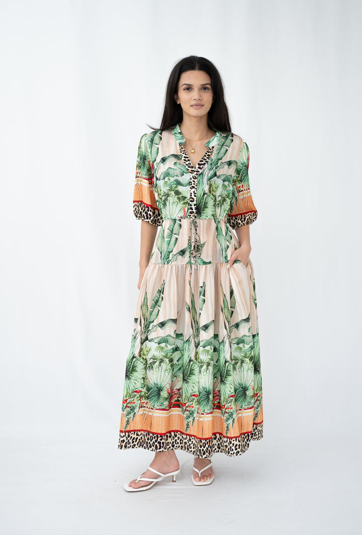 Woman wearing a tropical green palm-print midi dress with leopard trim and short sleeves, standing against a white background