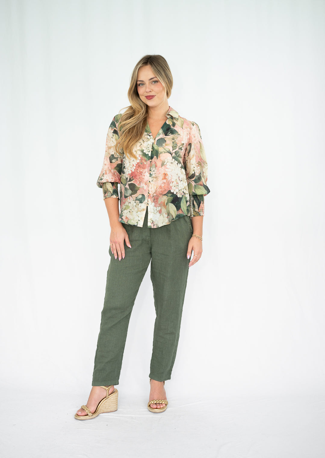 Woman wearing a floral blouse and green pants on a white background