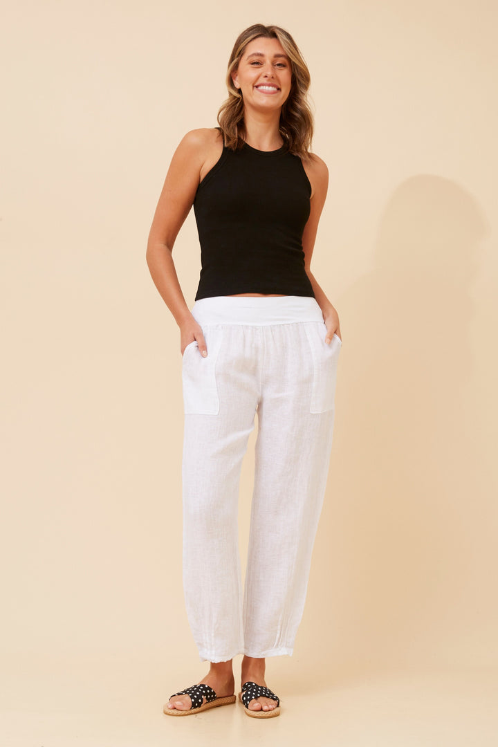 Woman wearing a black sleeveless top and white pants on a beige background