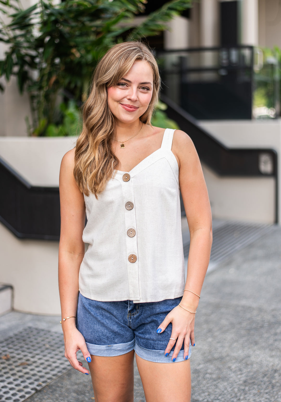 Woman wearing a white sleeveless button-up top and denim shorts standing outdoors.
