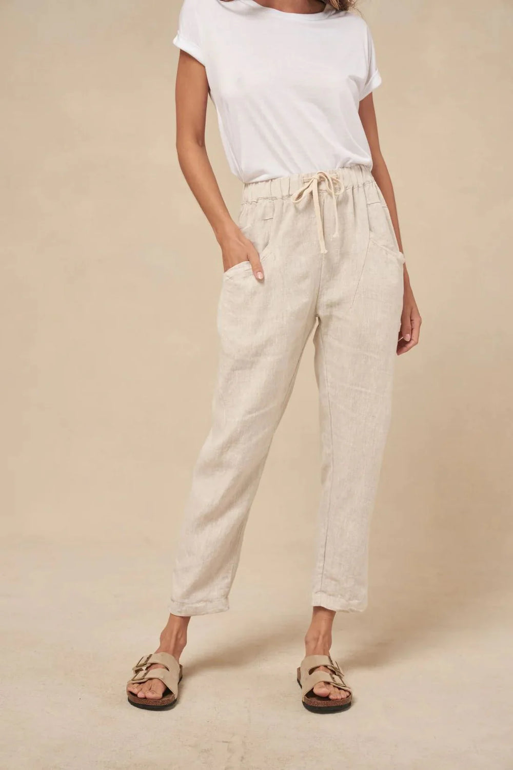Person wearing a white t-shirt and beige pants against a beige background