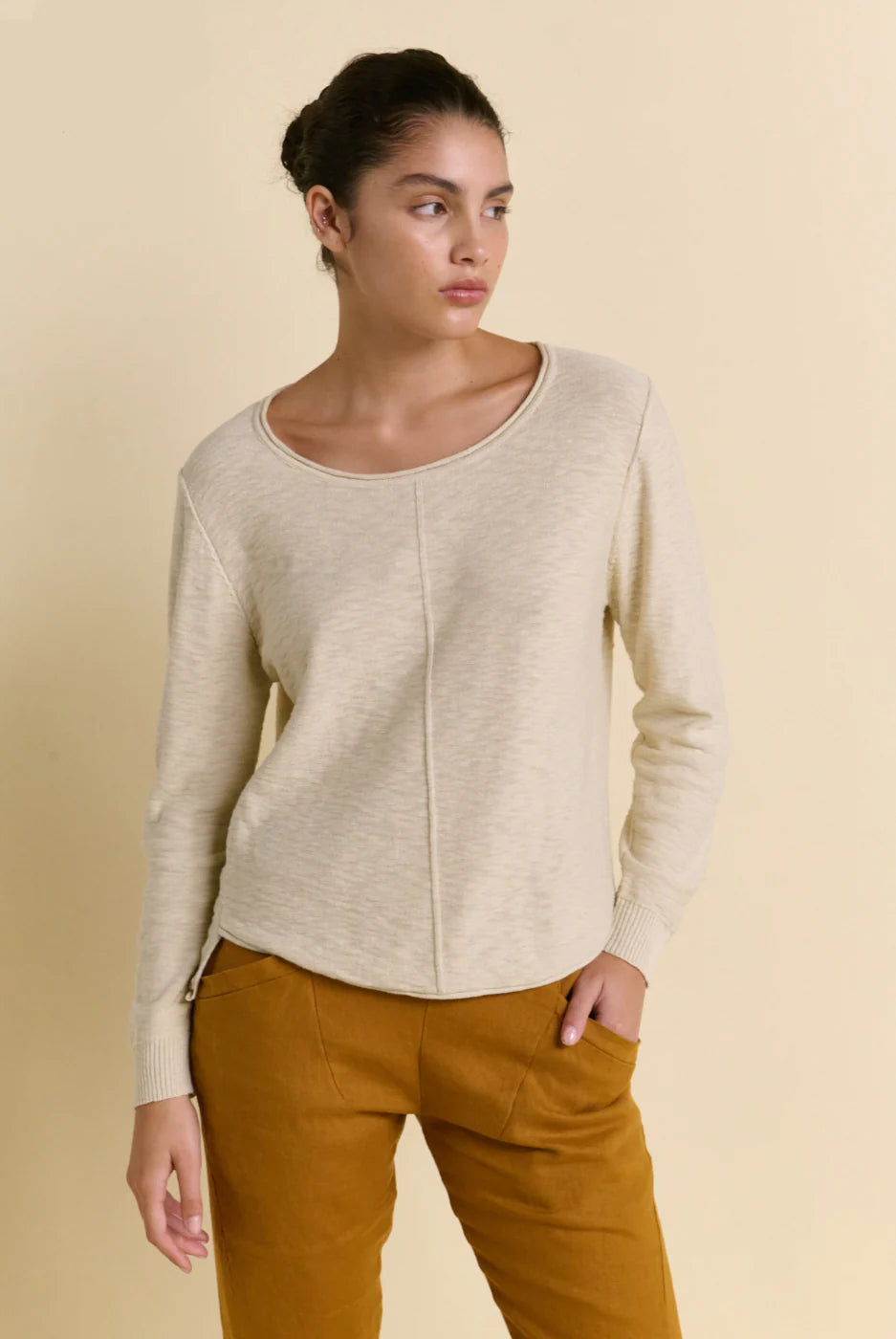 Woman wearing a beige sweater and brown pants against a beige background