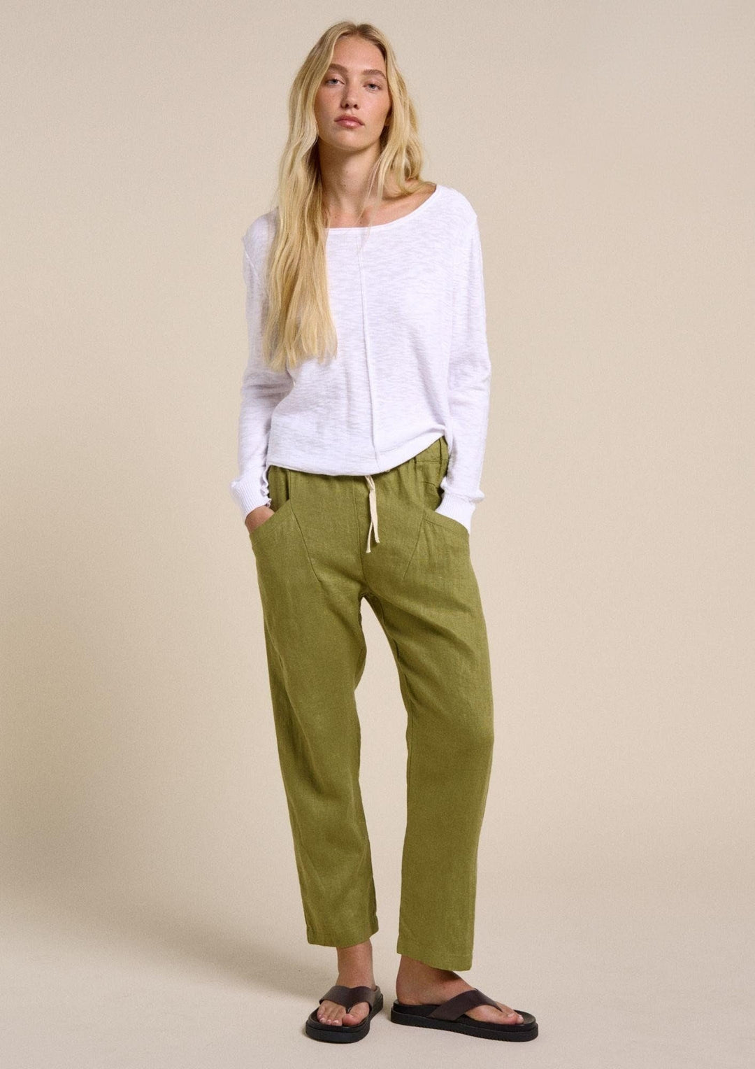 Woman wearing a white top and green pants against a beige background