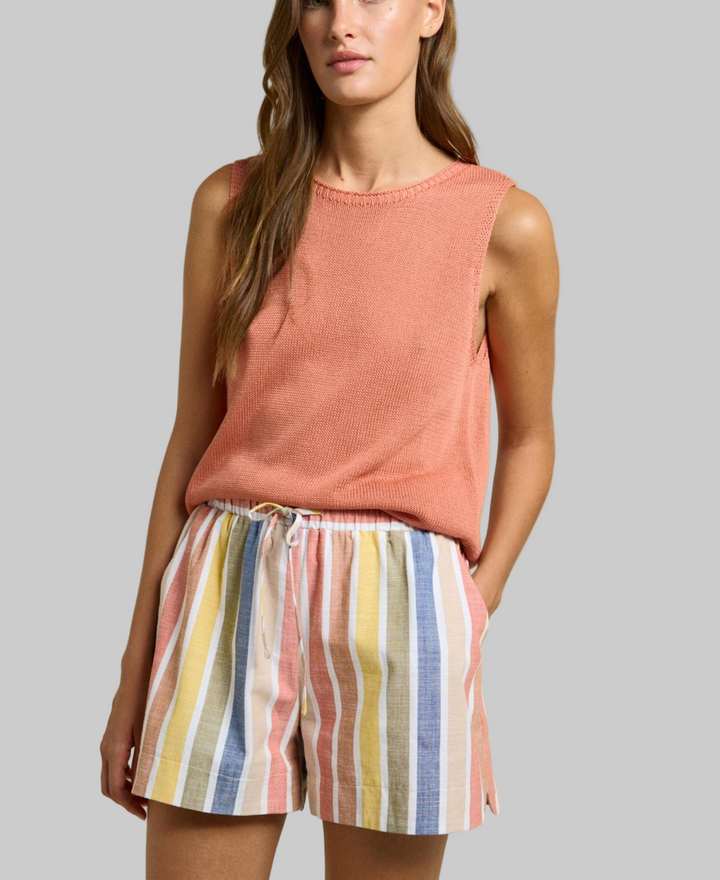 Woman wearing a pink sleeveless top and colorful striped shorts on a beige background