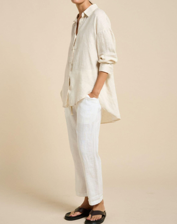 Person wearing a loose-fitting white shirt and pants against a beige background