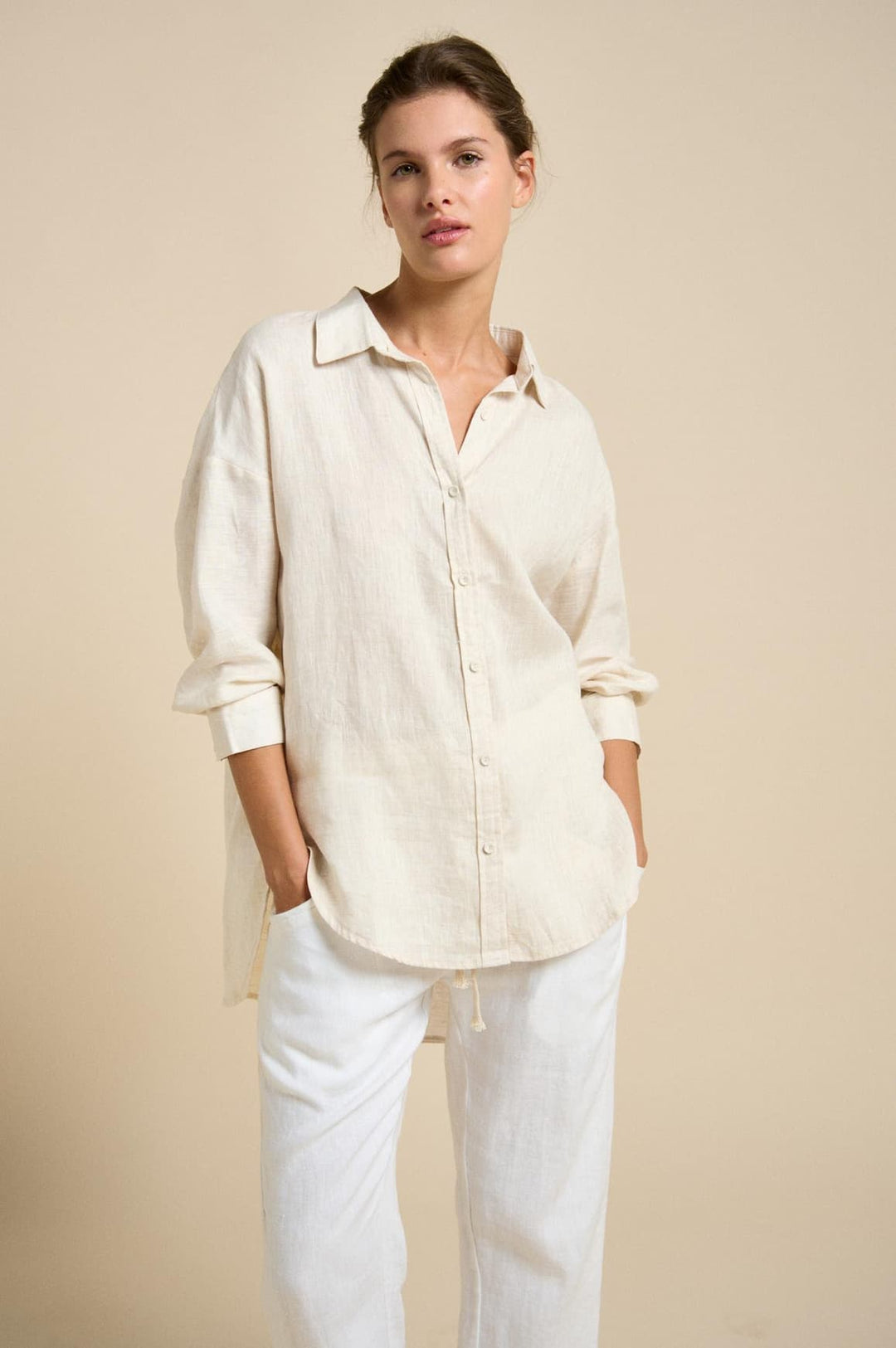 Woman wearing a light-colored shirt and pants against a beige background
