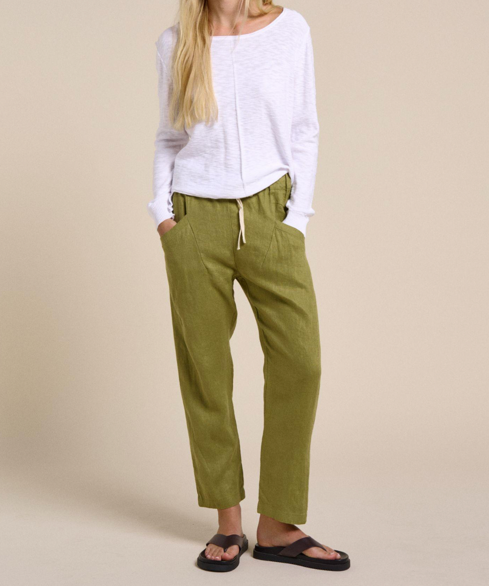 Person wearing green pants and a white top on a beige background