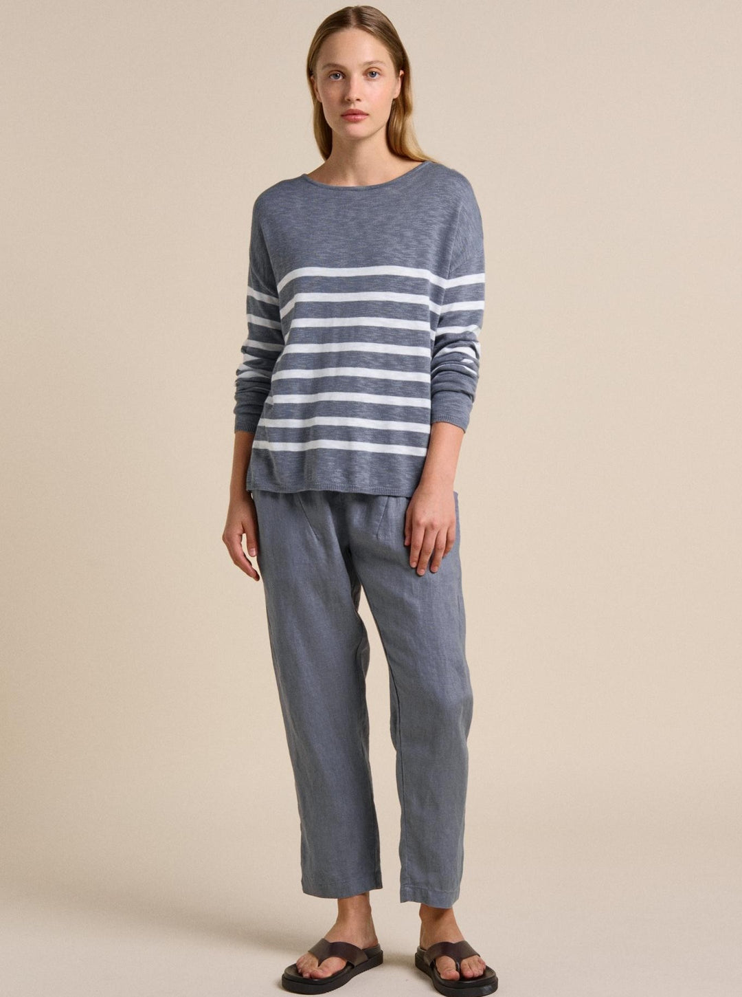 Woman wearing a blue and gray striped sweater and pants on a beige background