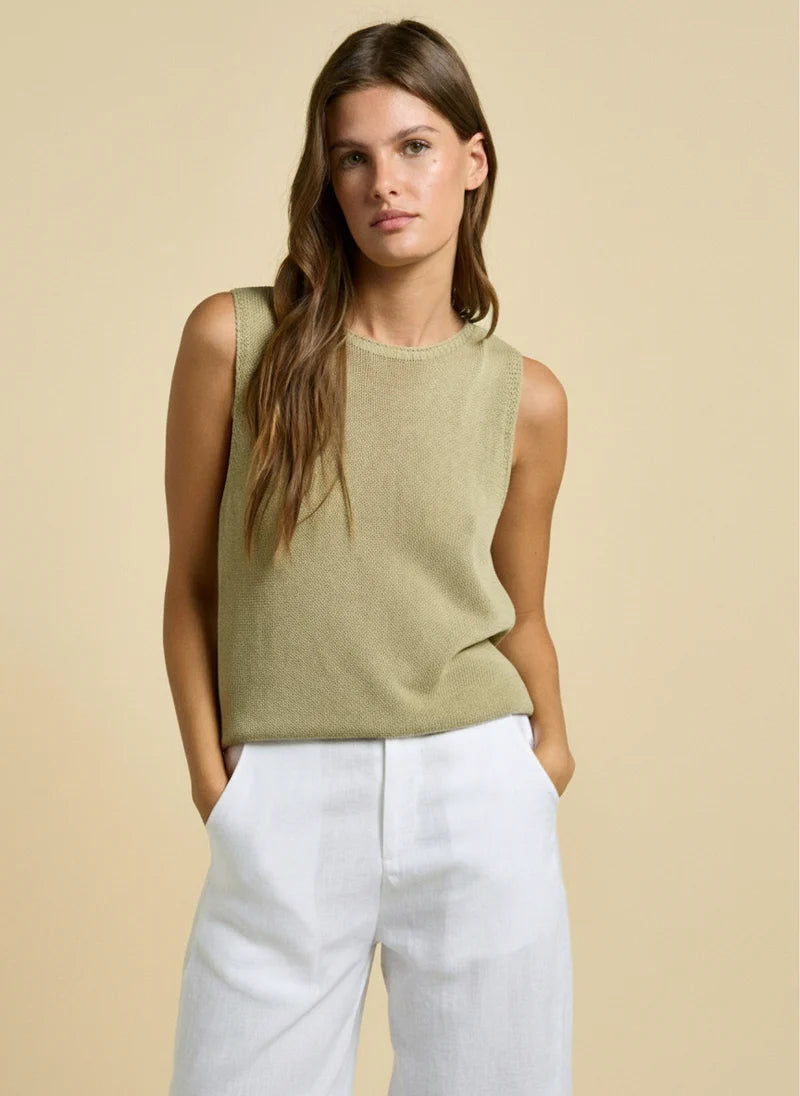 Woman wearing a green sleeveless top and white pants against a beige background