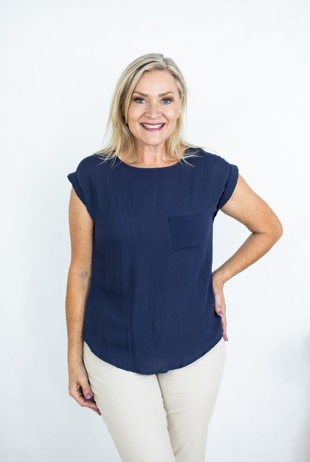A woman smiling and wearing a navy t-shirt with cuffed sleeves and a curved hem, paired with light pants.