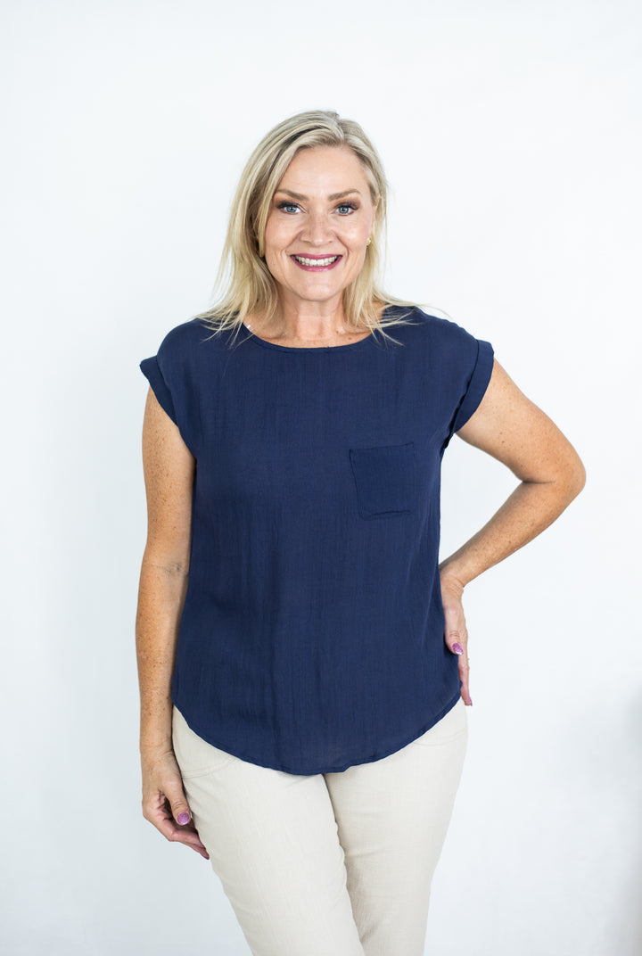 A woman smiling and wearing a navy t-shirt with cuffed sleeves and a curved hem, paired with light pants.
