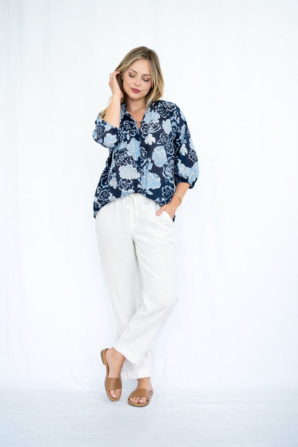 Woman wearing a blue floral blouse and white pants on a white background